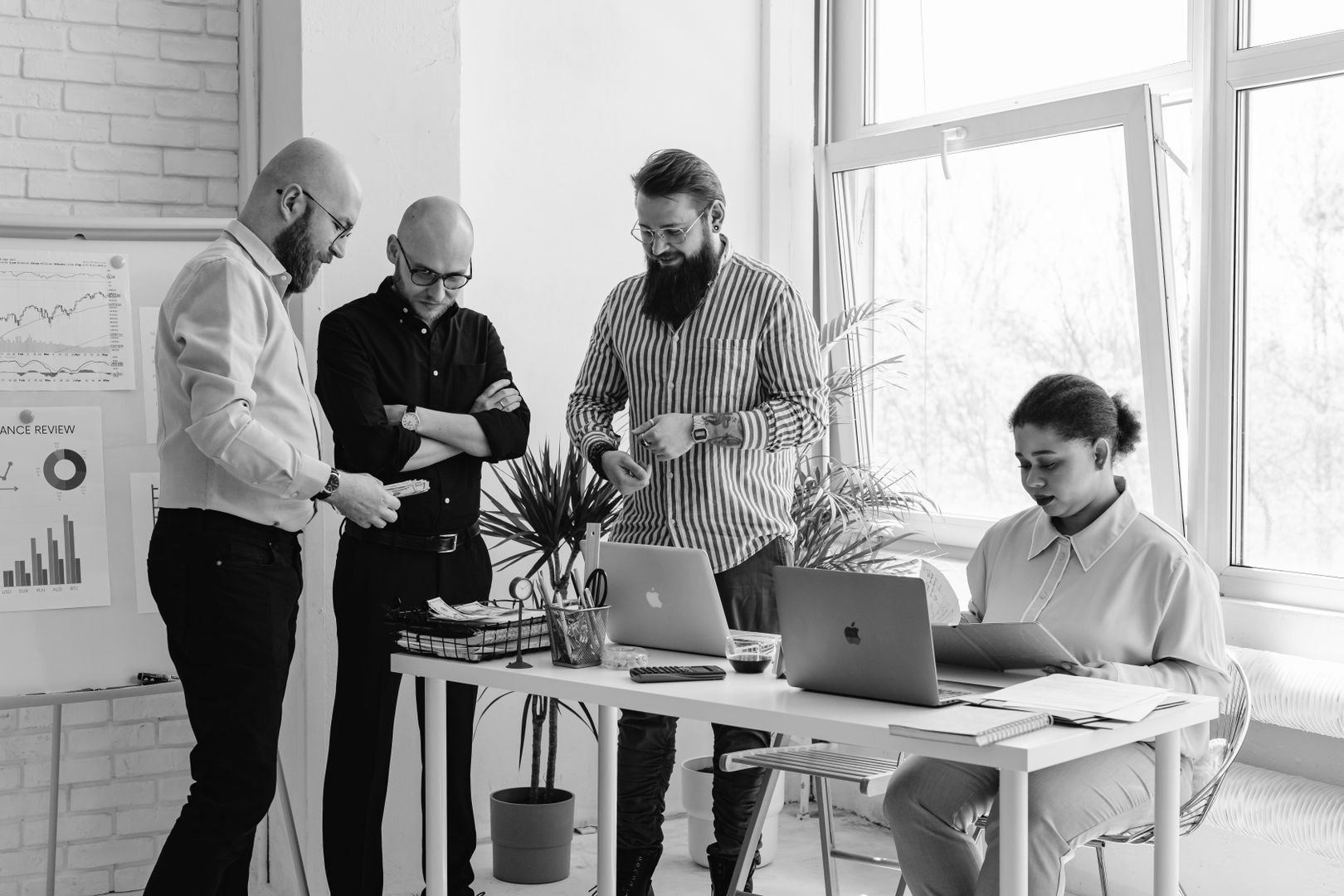 Four colleagues reviewing performance data together at a table with laptops in a bright, brick-walled office.