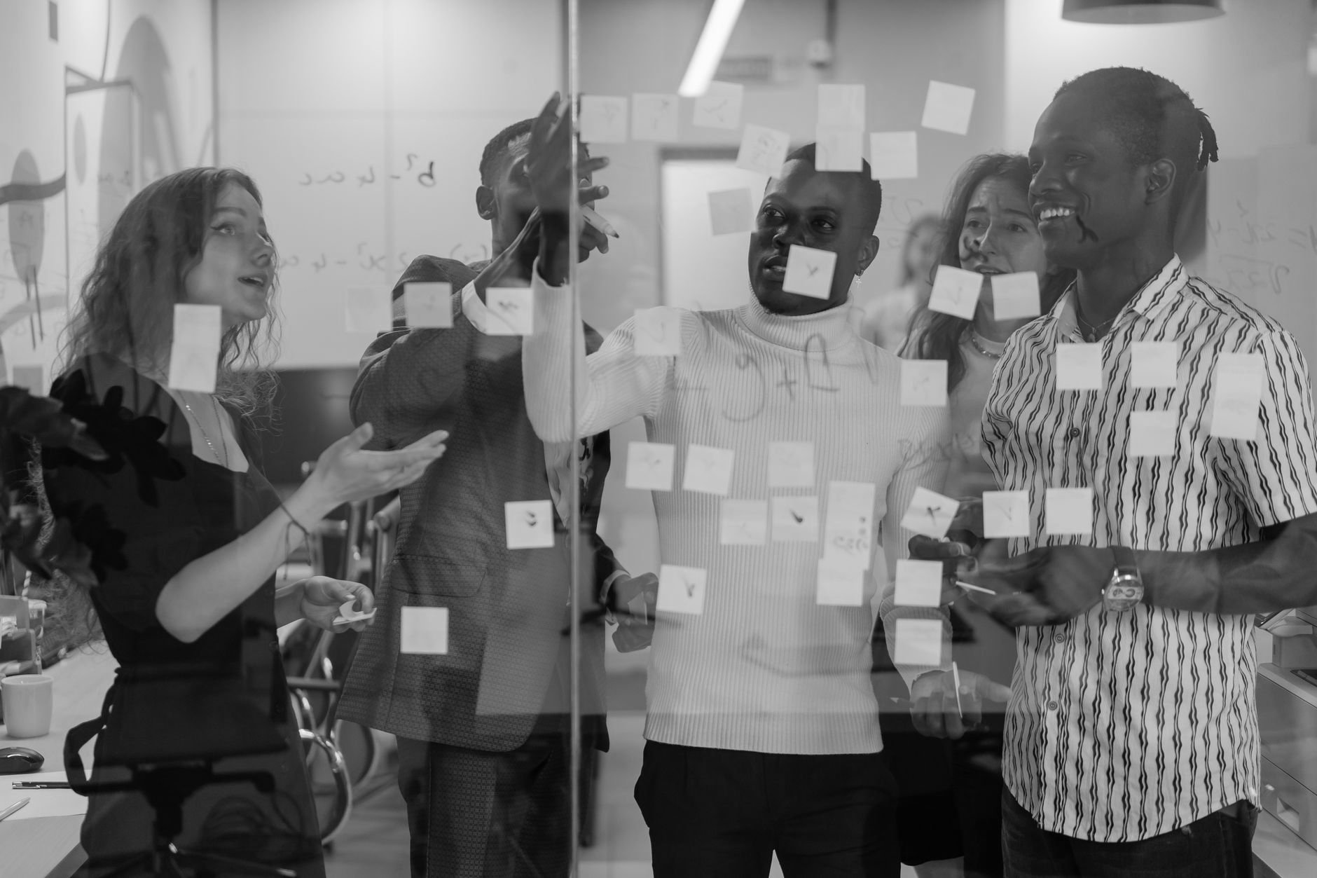 Colleagues mapping ideas with sticky notes on a glass wall during a working session
