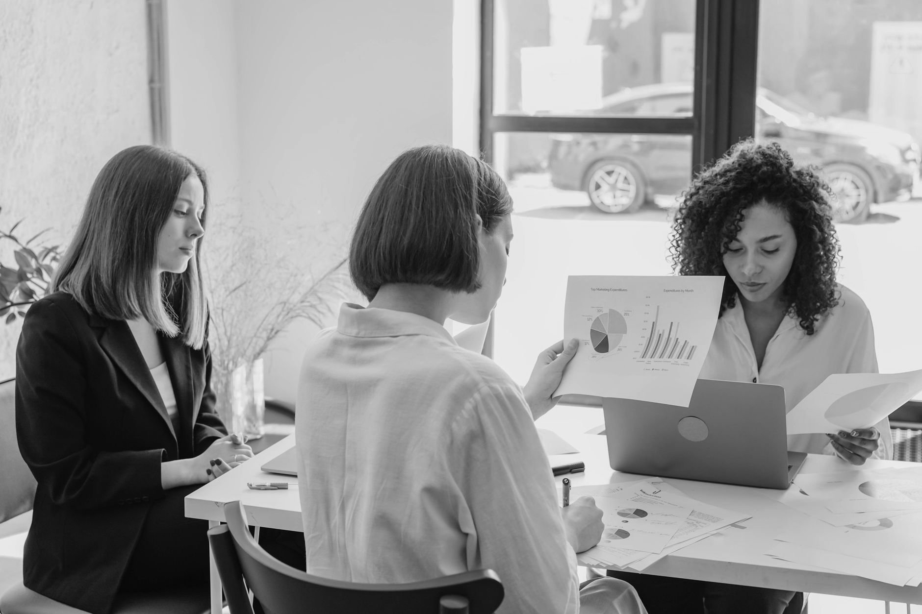 Three colleagues reviewing charts and a status report together at a table in a bright office